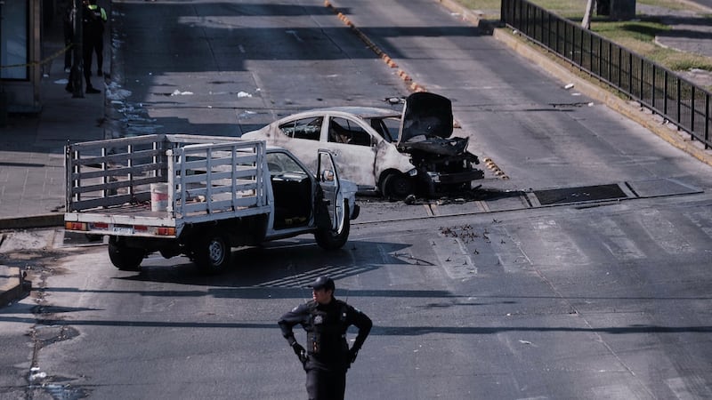 Un policía observa un vehículo calcinado que fue incendiado en una carretera de Guadalajara,...